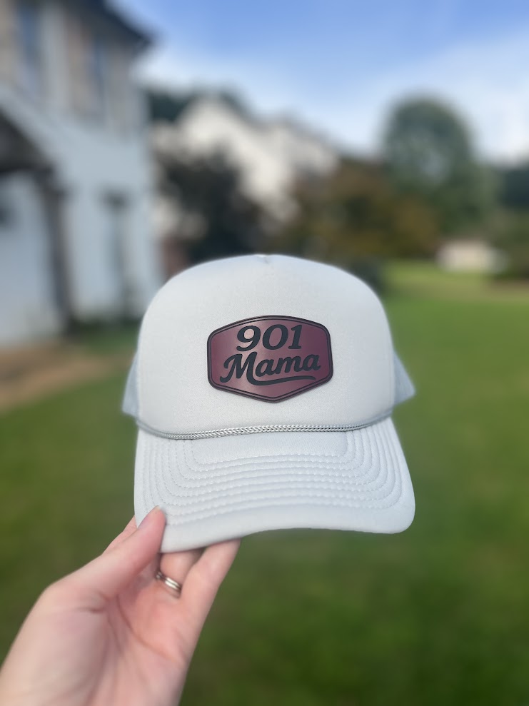 White cap with '901 Mama' patch held in front of a blurred outdoor background